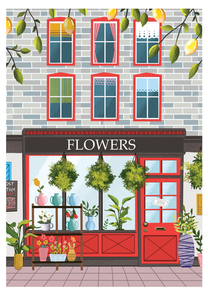 Charming illustration of a flower shop with a red door and large front windows displaying various potted plants and colorful vases. Hanging plants are suspended above the display, and a small 'open' sign hangs on the door. The building has a gray brick facade with red-framed windows on the upper floors, each with different curtains. Lemon tree branches with lemons hang above, adding a touch of greenery to the scene.